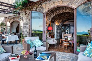 An outdoor seating area with stone walls, wicker furniture, and a view of the sea. - Lubra Casa Relax (Massa Lubrense)