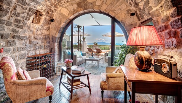 A cozy room with stone walls, a wooden table, a wicker armchair, a sofa, and a radio.