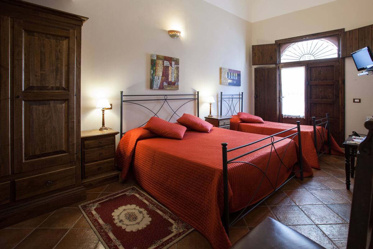 A bedroom with two beds, wooden furniture, a red rug, and artwork on the walls.