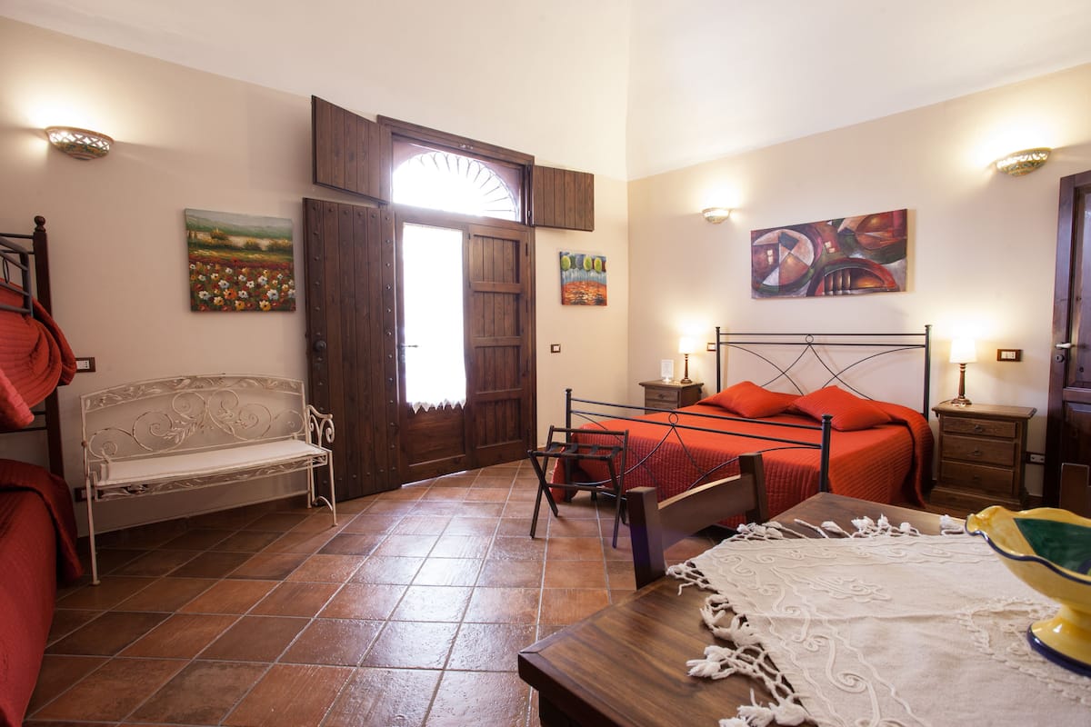 A bedroom with a bed, bench, table, and artwork on the walls.
