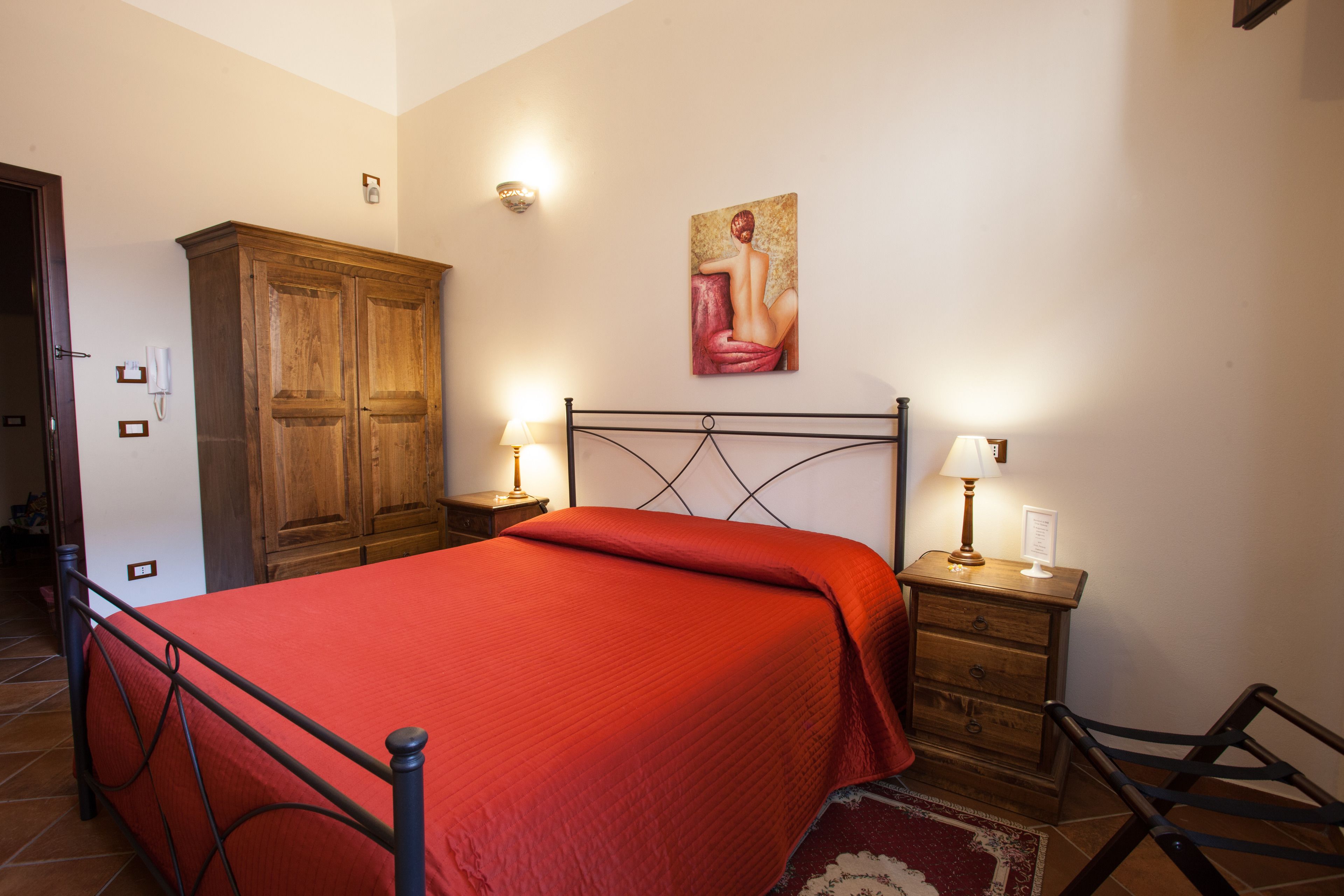 Un dormitorio con cama, armario de madera, dos mesitas de noche con lámparas y un cuadro en la pared.