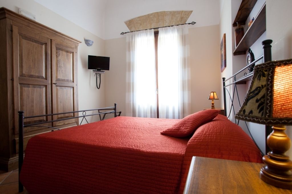A bedroom with a bed, a television, a window with curtains, and a lamp.