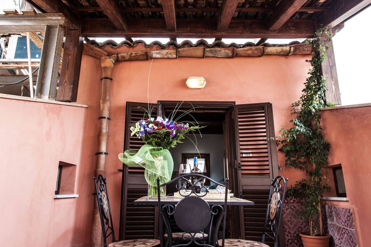 A covered patio with a wooden ceiling, a table with four chairs, and a potted plant.