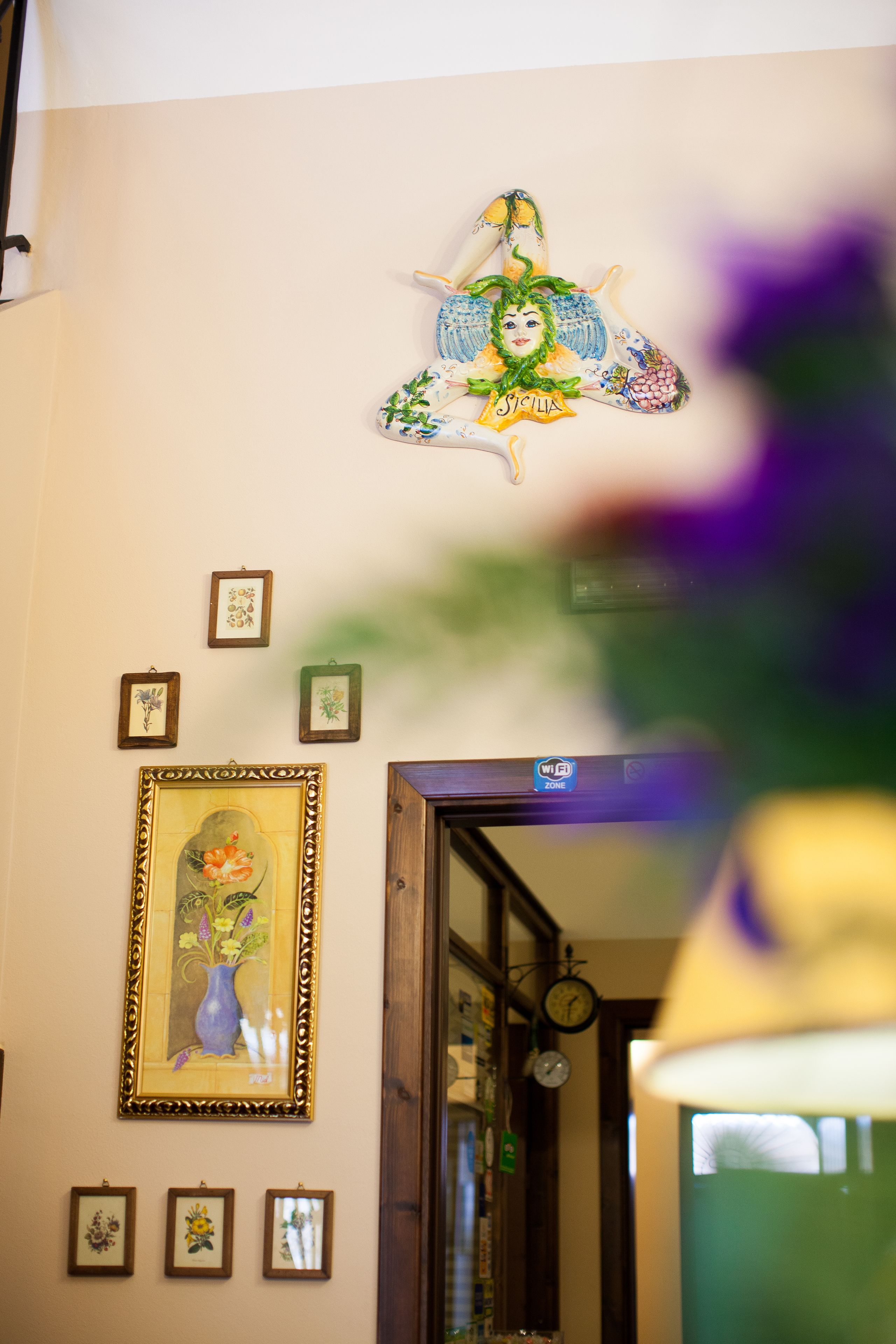 A room with a wall decorated with framed artwork, a clock, and a hanging ornament.