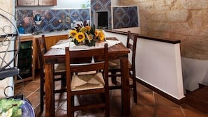 A rustic kitchen with wooden beams, a stone wall, and a dining area with a table set for two. - Cinisi Vacanze (Cinisi)