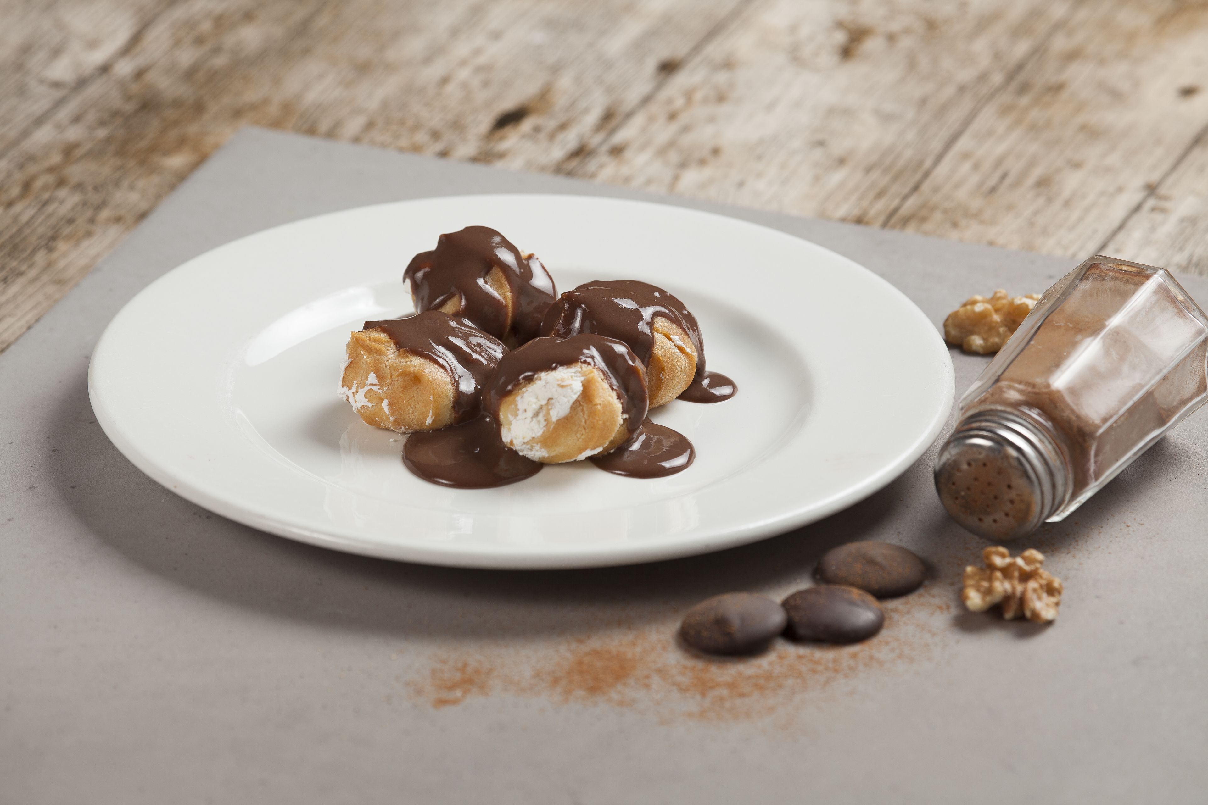 A plate of chocolate-covered pastries on a white plate with a wooden table background.