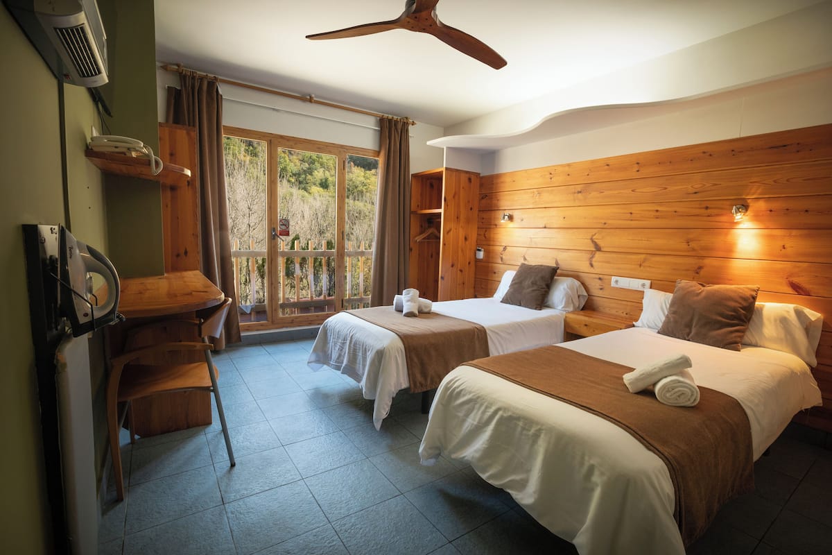 A hotel room with two beds, a desk, a chair, and a large window with curtains.