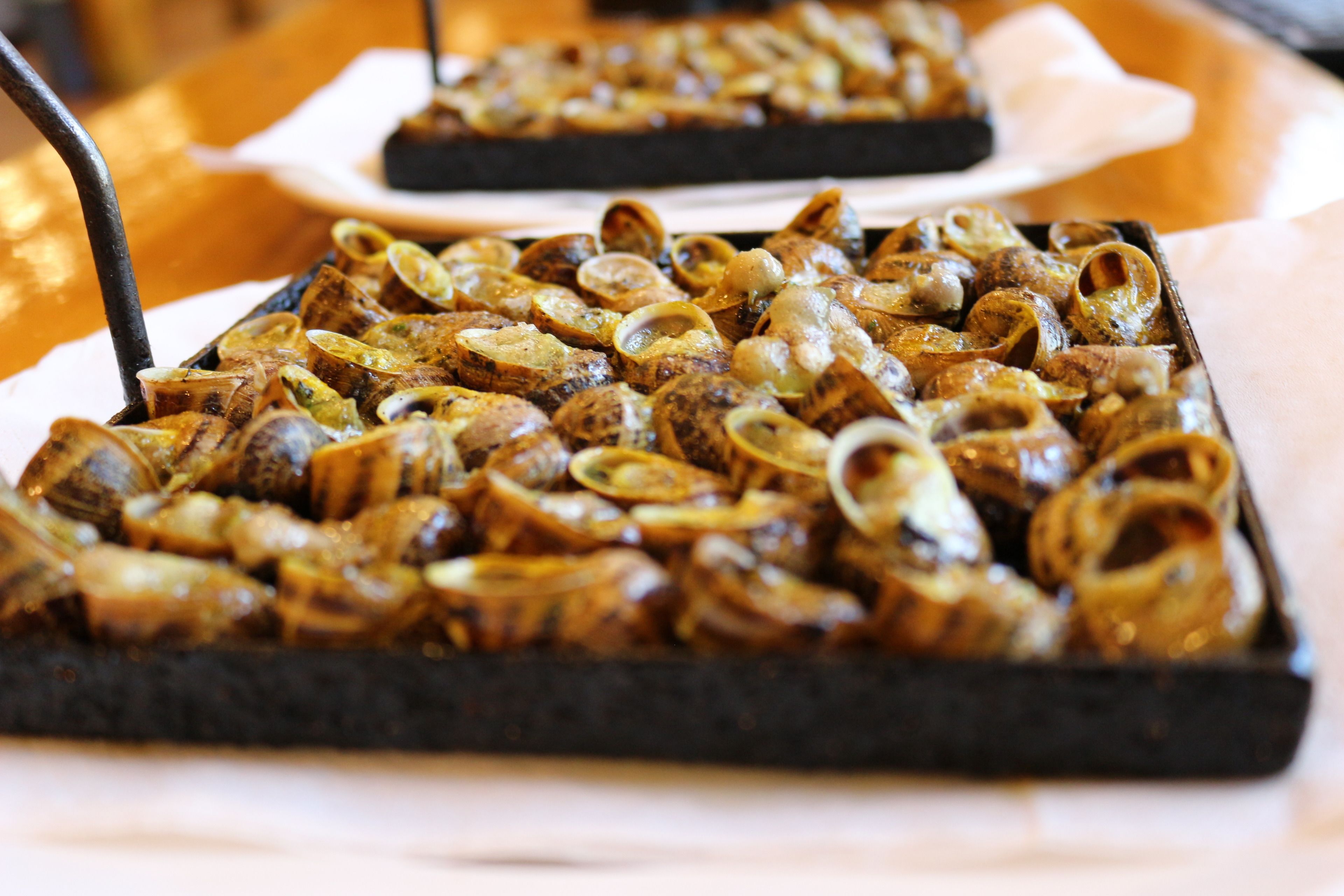 A tray of cooked shellfish, possibly clams, served on a black tray.