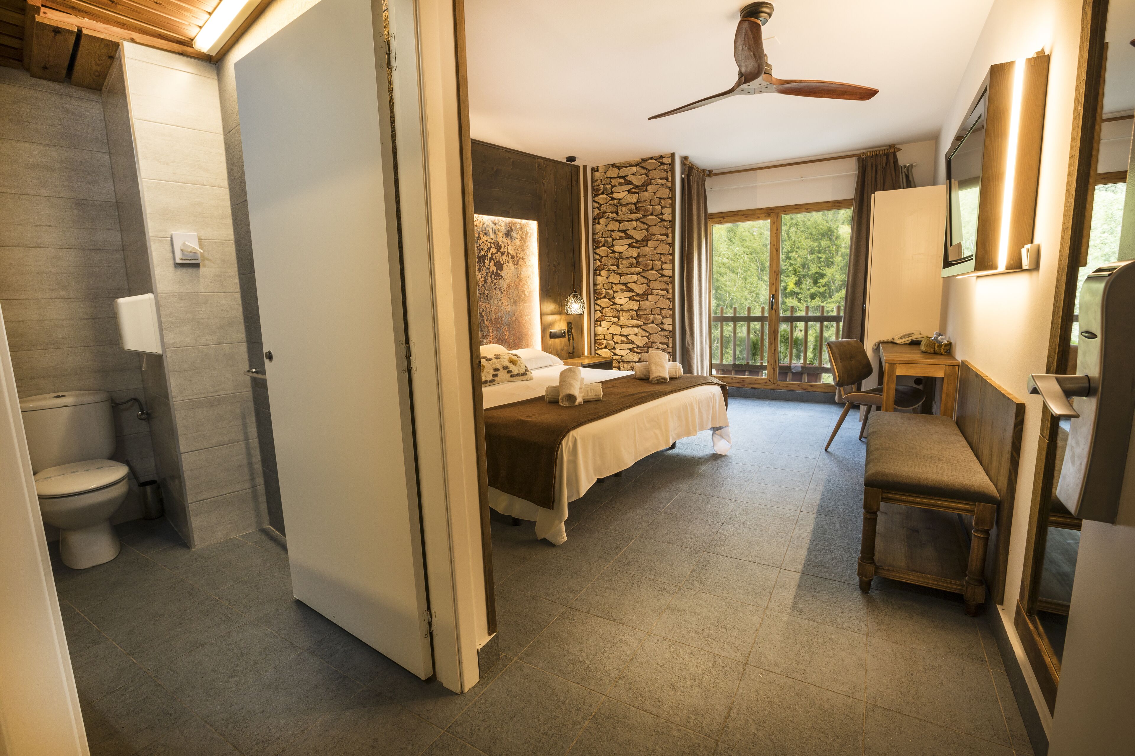 Un dormitorio con cama, escritorio, silla, pared de acento de piedra y una ventana grande.