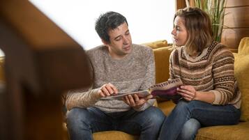 Two people sitting on a couch, reading a magazine.