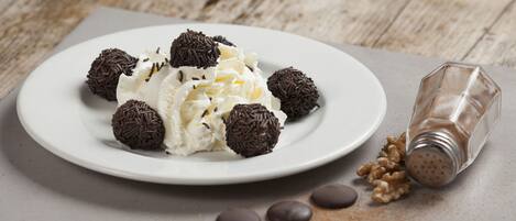 A plate of whipped cream with chocolate balls and a salt shaker on a wooden table.