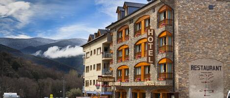 Un hotel con varios balcones, un restaurante y vistas a montañas.