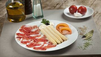 Un plat amb talls de carn, palets de pa i tomàquets sobre una taula de fusta.