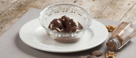 A clear glass bowl with chocolate-covered ice cream on a white plate, accompanied by scattered walnuts and a salt shaker.