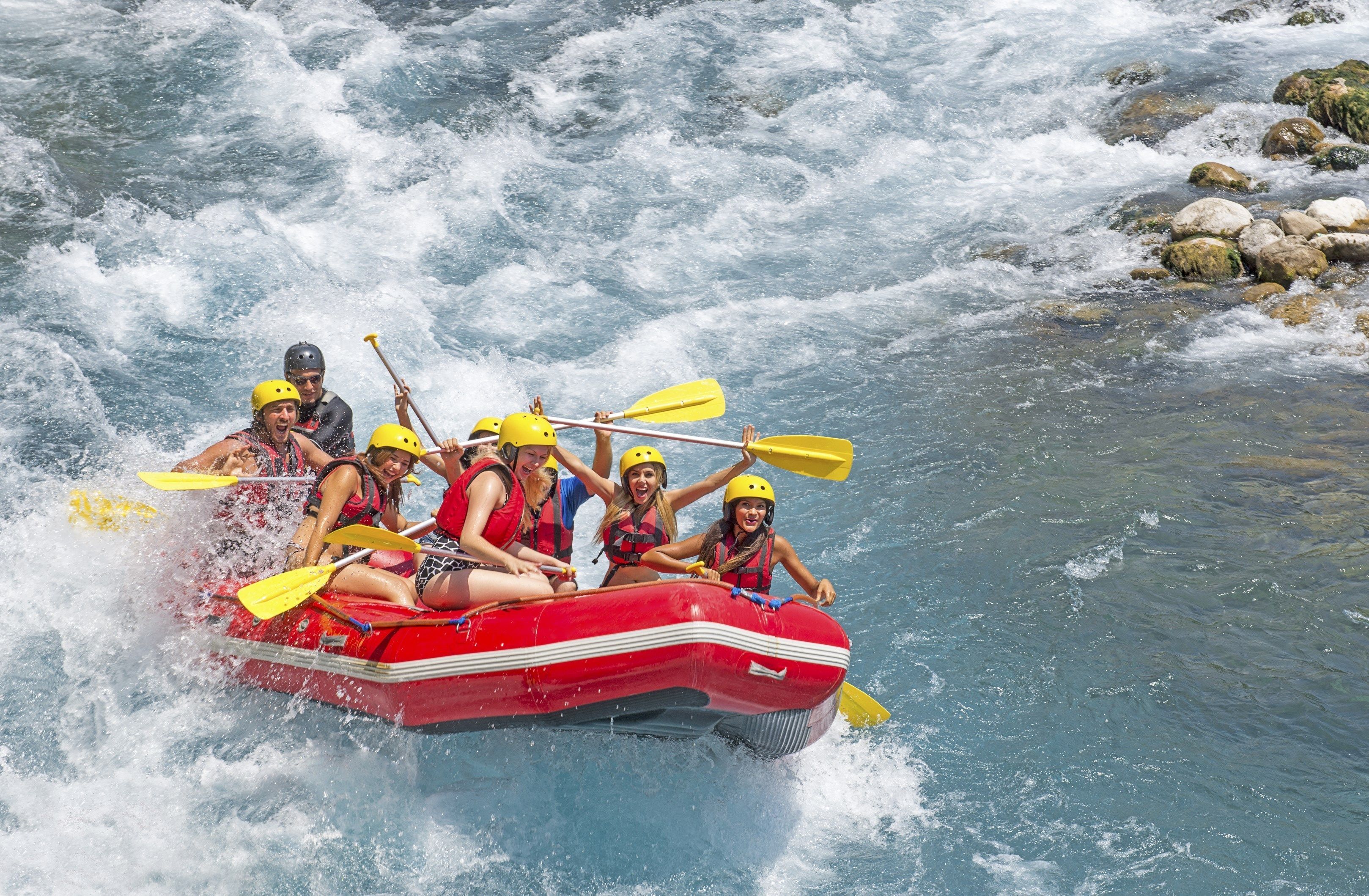 Un grupo de personas en una balsa roja con remos amarillos navegando por un río con rocas.