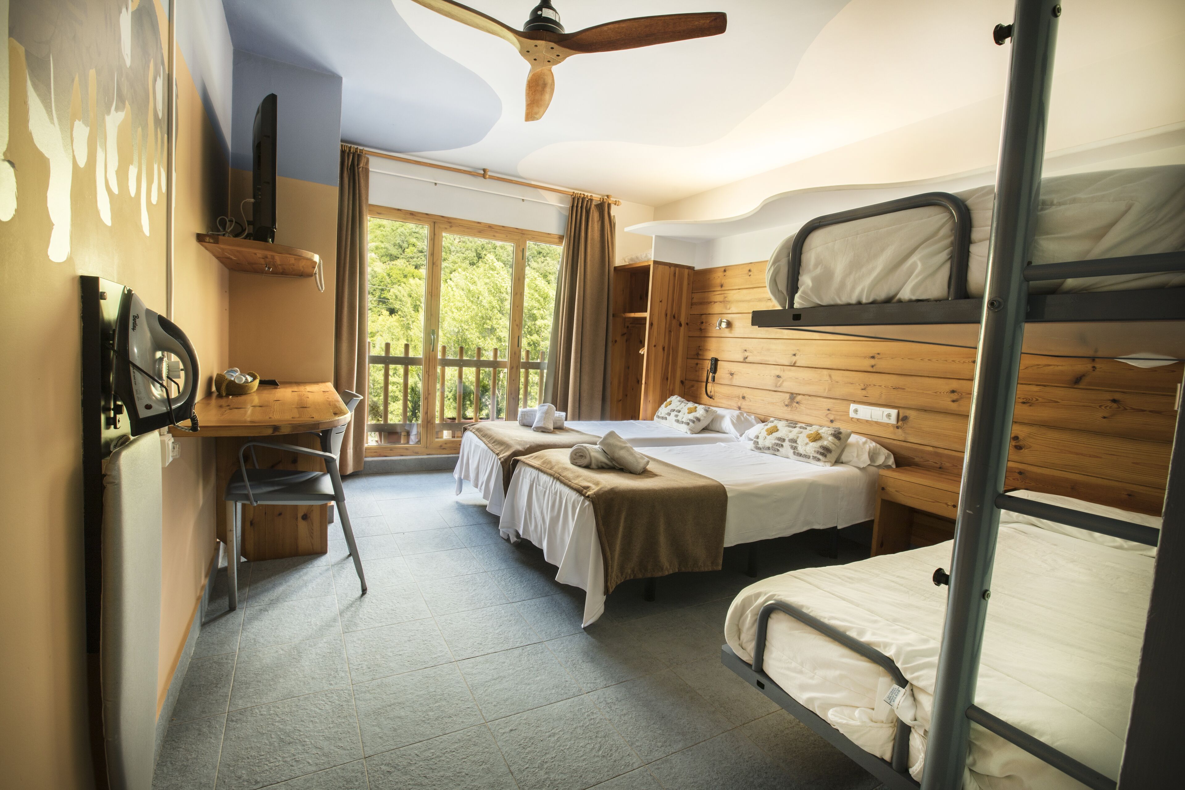 A room with bunk beds, a desk with a chair, a television, and a window with curtains.