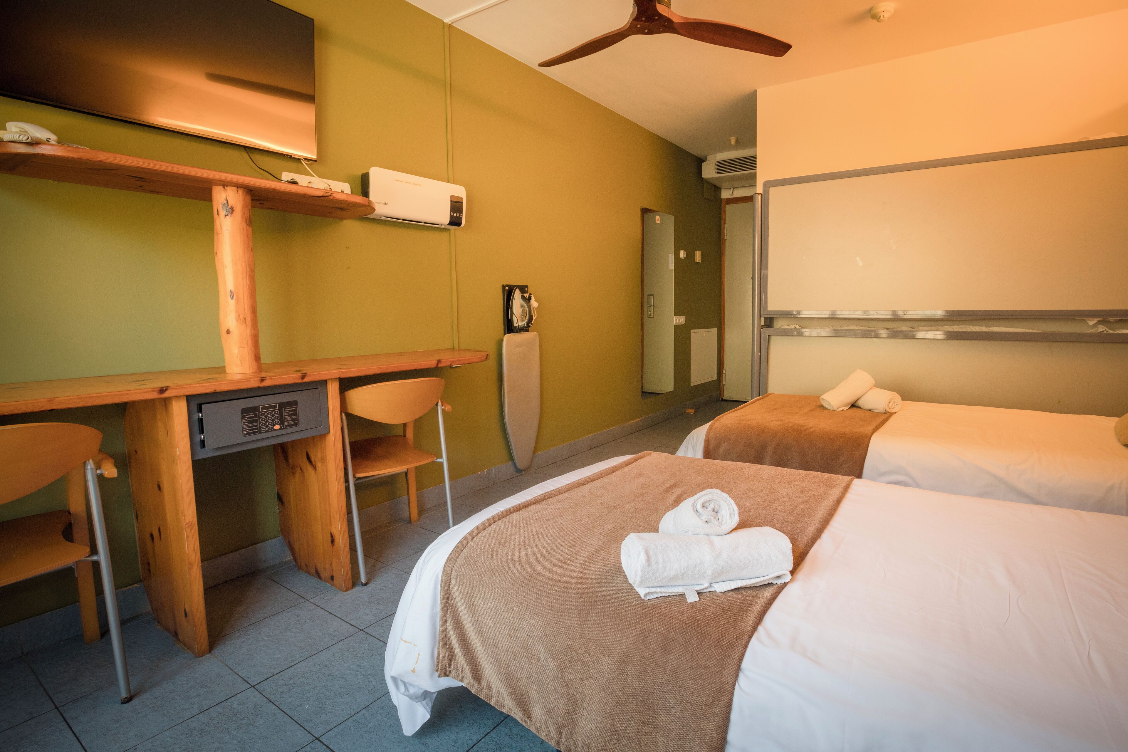 Una habitación de hotel con dos camas, un escritorio, una silla y un ventilador de techo.
