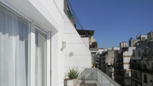 Uma varanda com uma cadeira verde, plantas em vasos e vista para edifícios vizinhos.