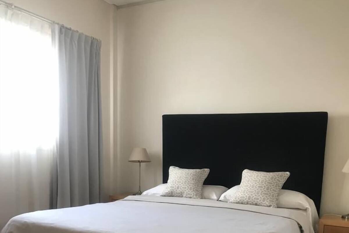 A neatly made bed with a dark headboard, two pillows, and a bedside table with a lamp.