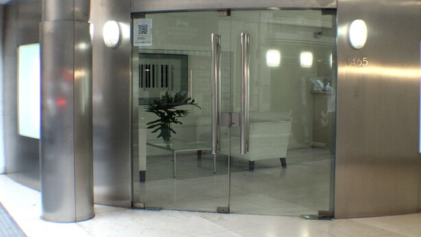 Um elevador moderno com porta de vidro, um vaso de planta e o número do andar 1465 visível.
