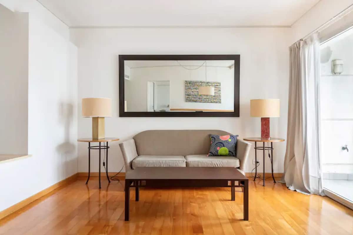 A modern living room with a sofa, a coffee table, two lamps, and a large mirror on the wall.