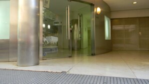 Entrada de um edifício moderno com porta de vidro, um pilar de metal e piso revestido de azulejos.