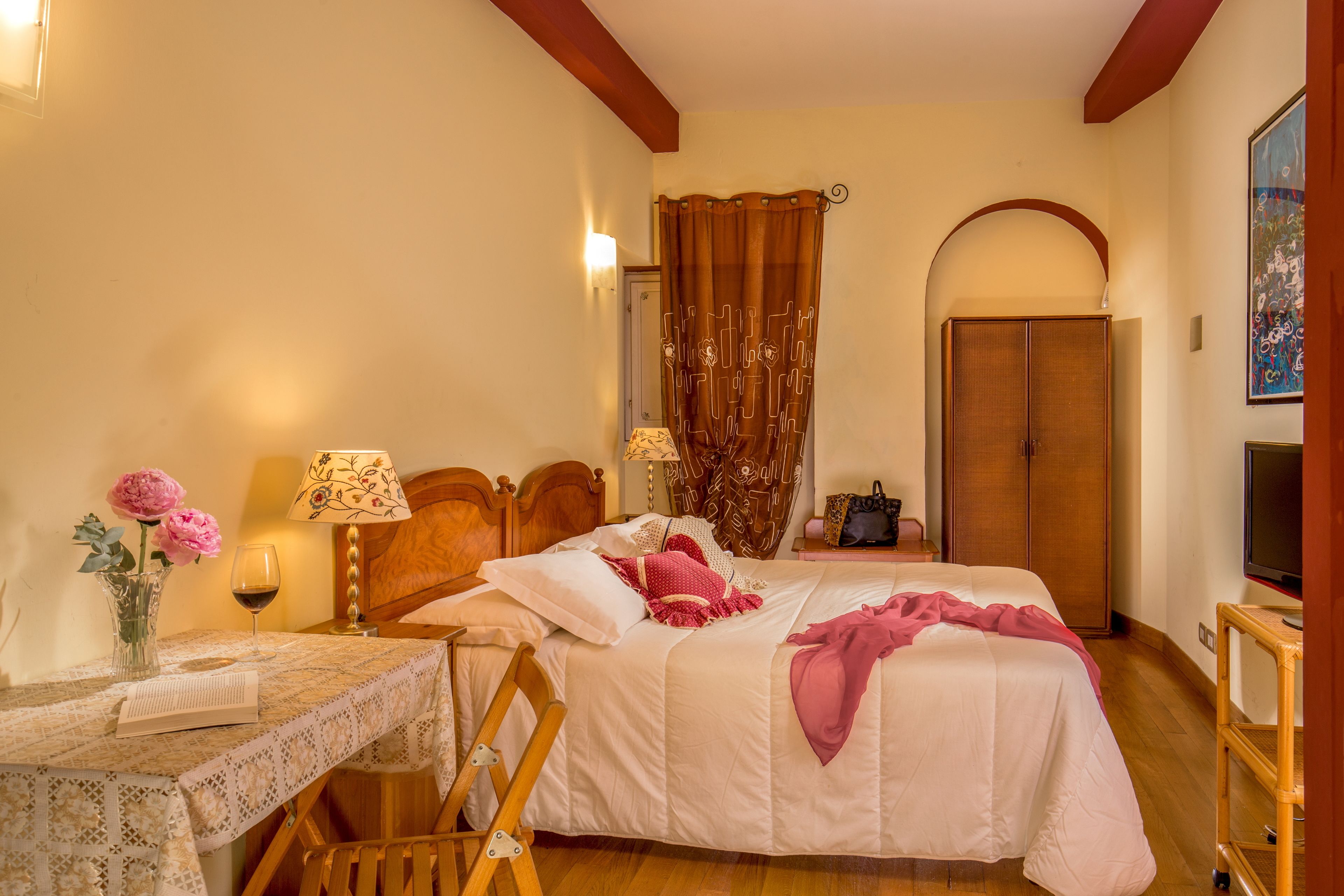 Une chambre à coucher avec un lit, une table de chevet, une lampe, des fleurs et un téléviseur.