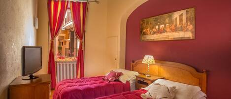 A room with two beds, a television, a painting, and a window with red curtains.