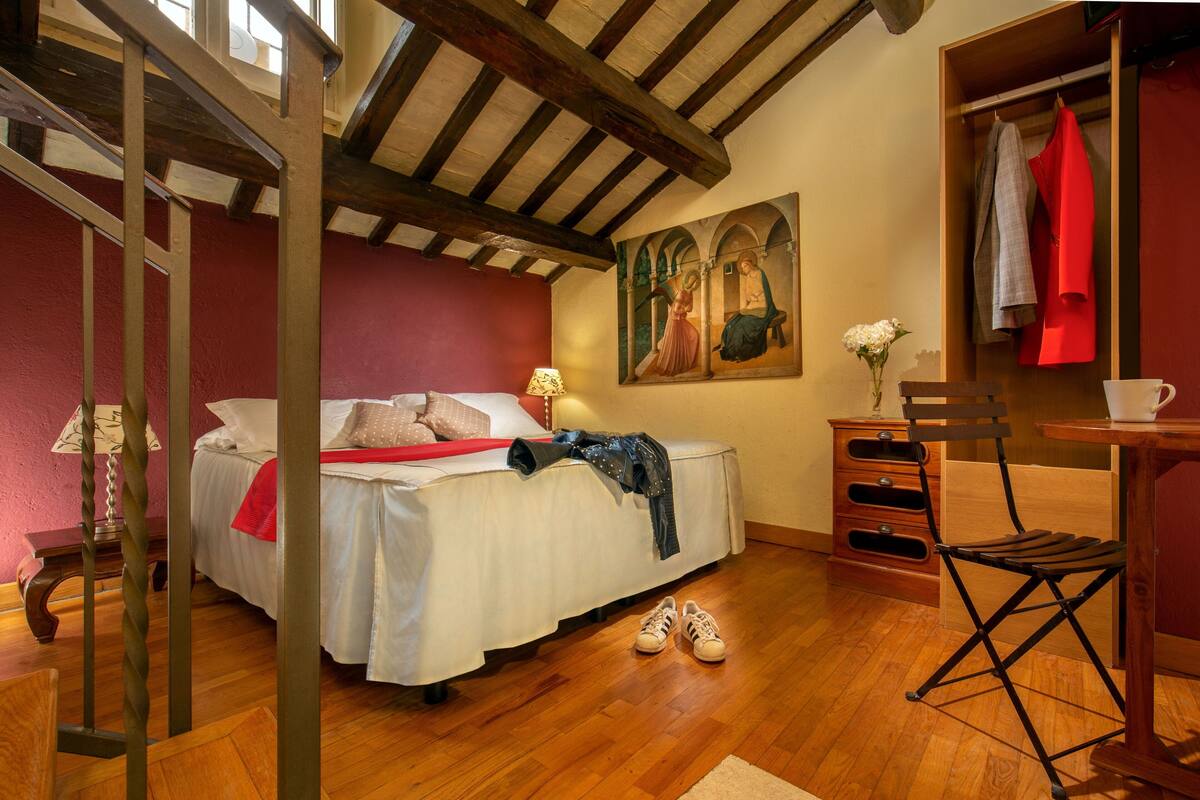 Une chambre à coucher avec un lit, un plancher en bois, un tableau, une chaise, une table et une armoire en bois.