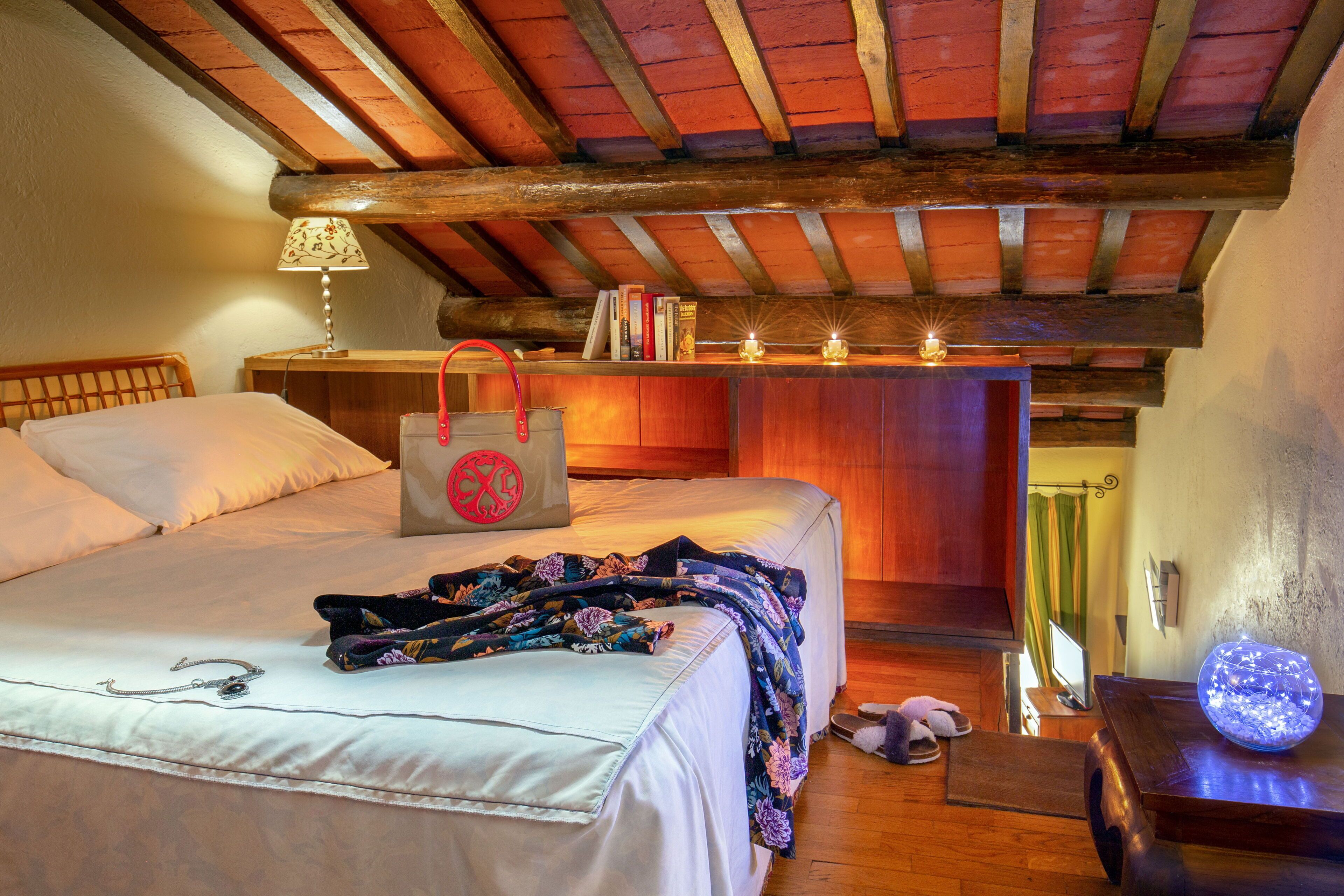 A bedroom with a wooden ceiling, a bed with a floral blanket, a bedside table with a lamp, and a nightstand with a decorative item.