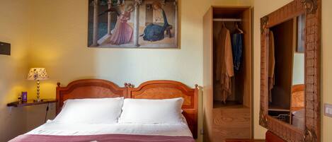 A neatly made bed with a book, a painting above it, and a mirror on the wall.
