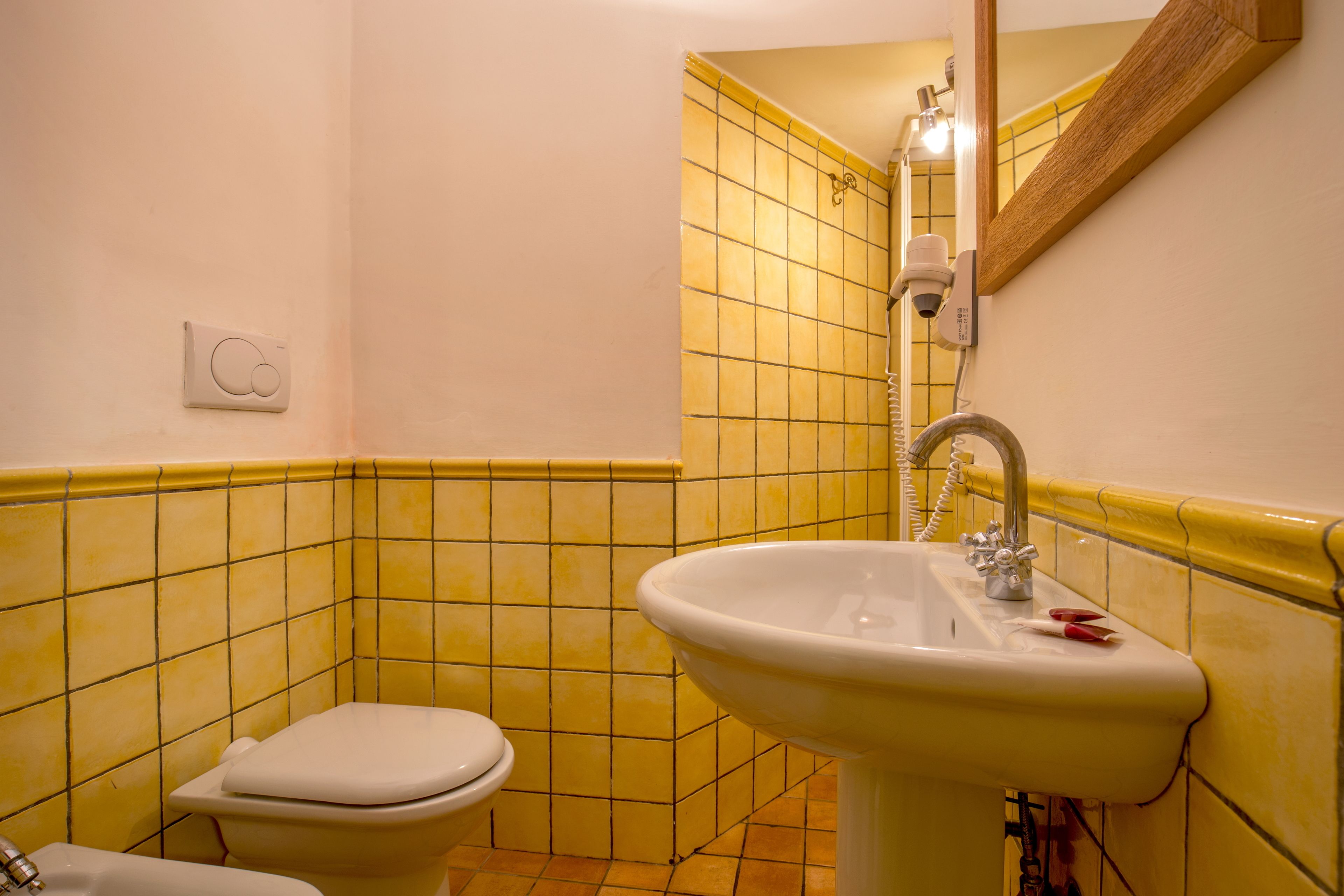 A bathroom with yellow tiled walls, a white sink, and a white toilet.