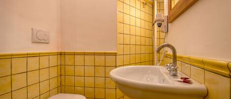 A bathroom with yellow tiled walls, a white sink, and a white toilet.
