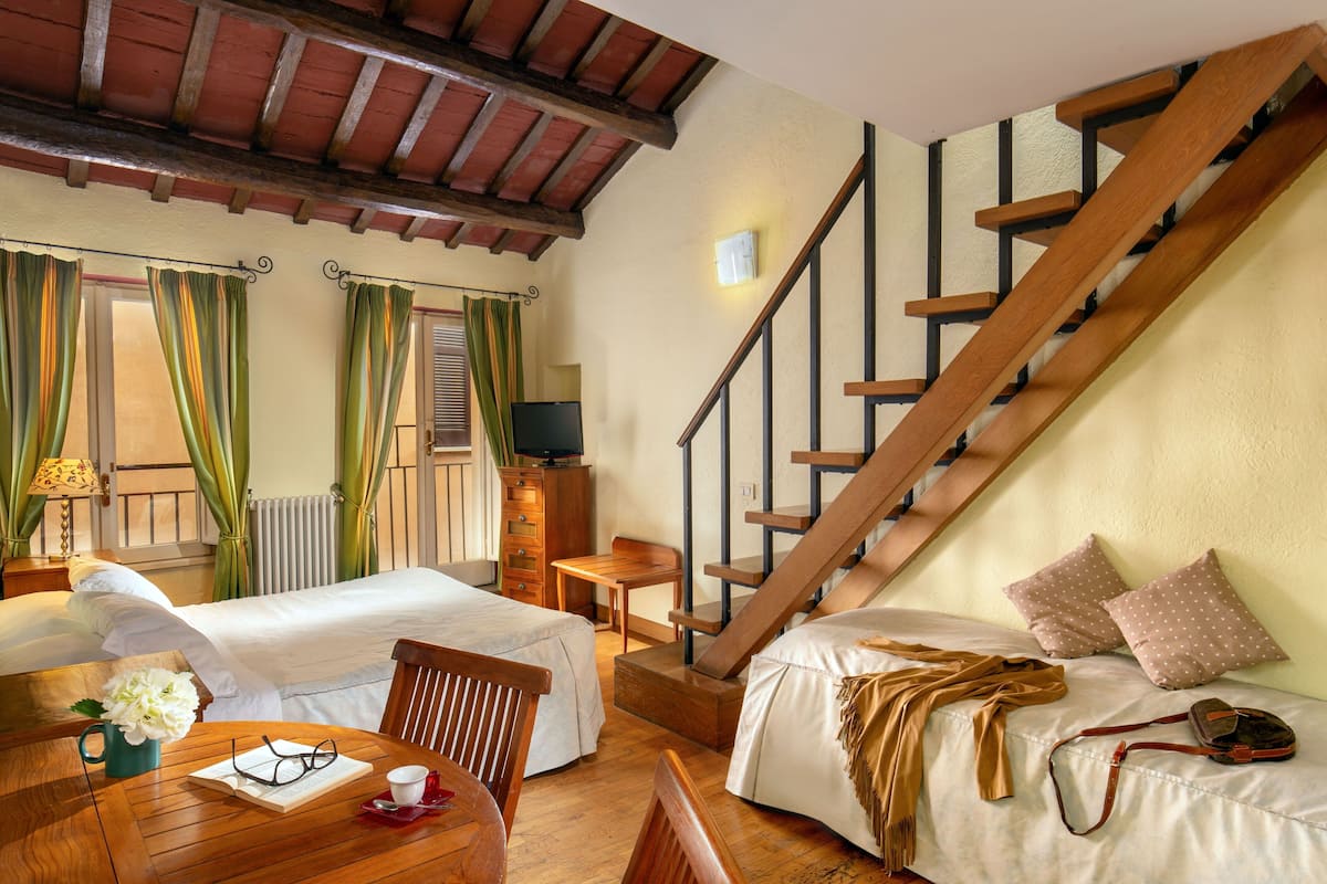Une chambre d’hôtel avec deux lits, un escalier en bois, une petite table avec une chaise, une lampe et un téléviseur.