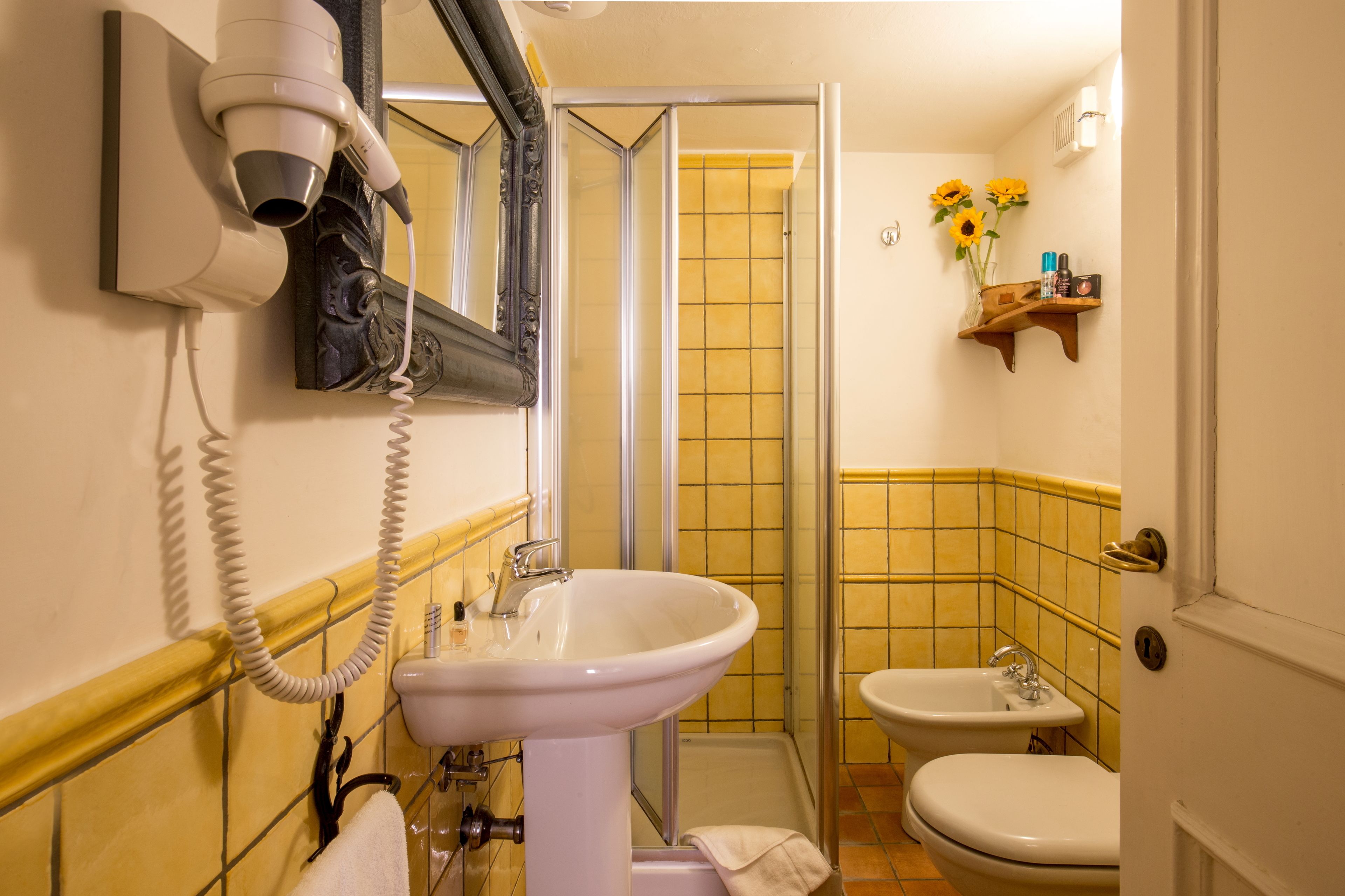 A bathroom with a white sink, a mirror, a hairdryer, a shower, and a shelf with toiletries.