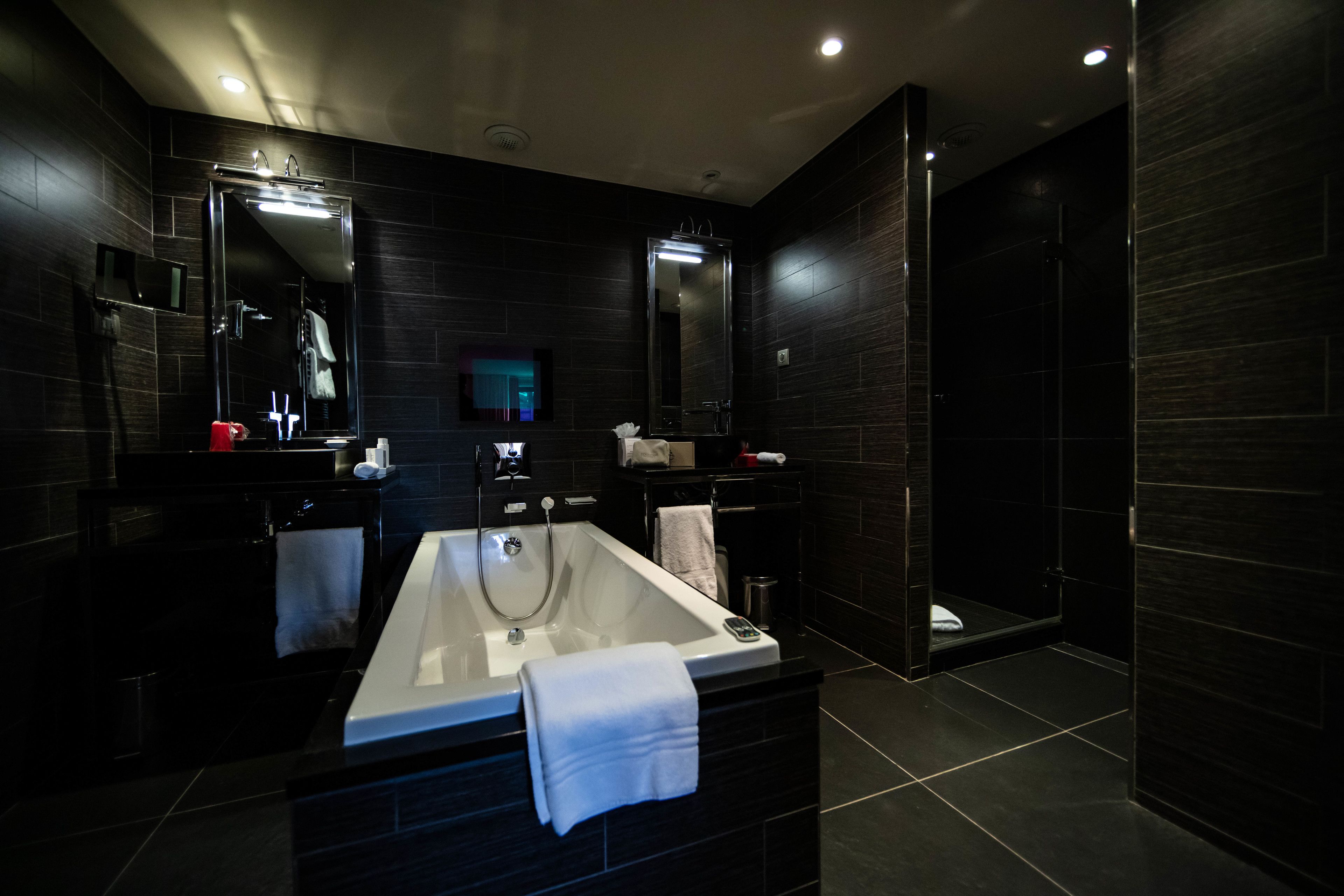A modern bathroom with a large bathtub, dark tiles, and two mirrors.