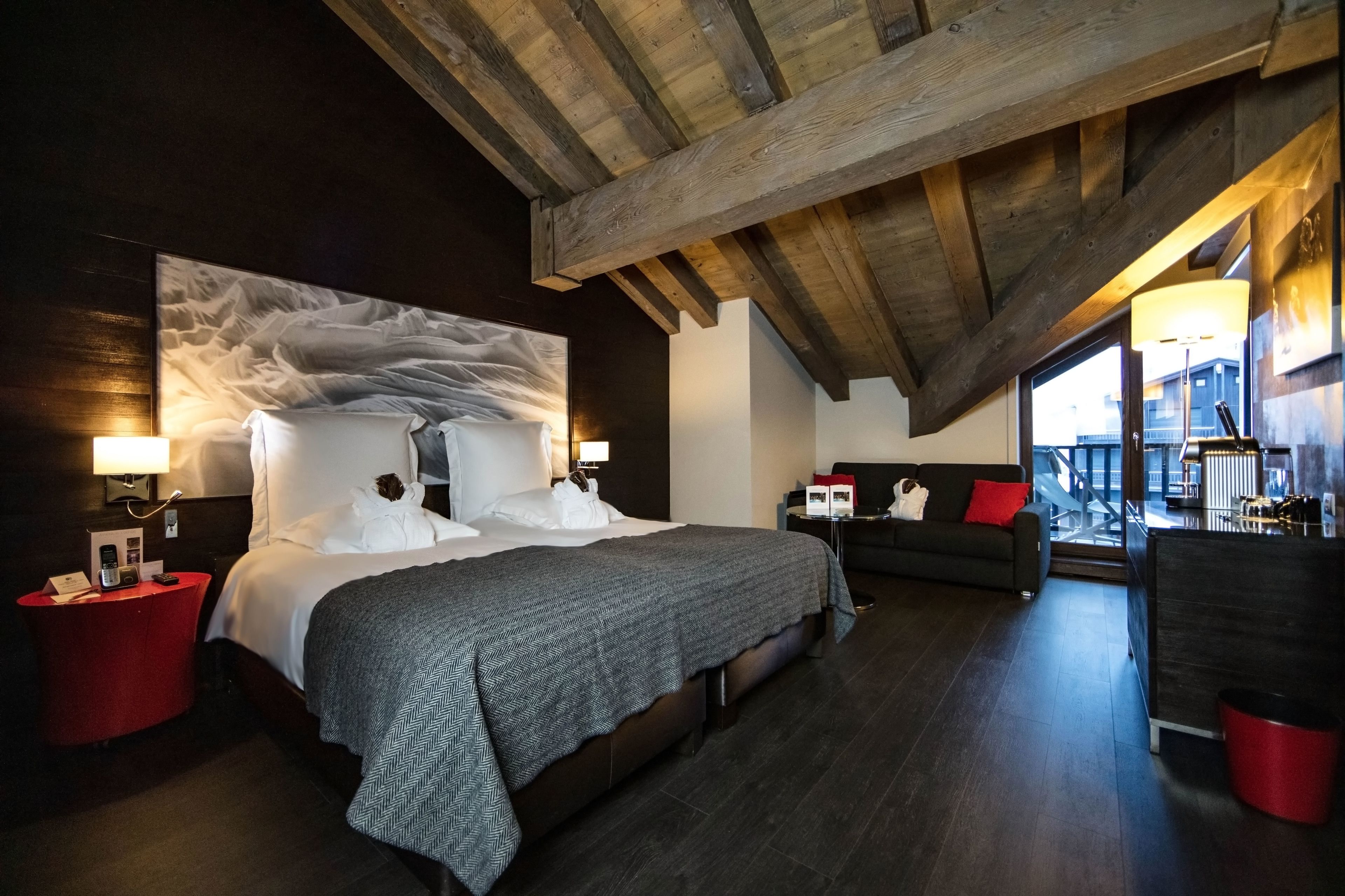 A modern bedroom with a large bed, a sofa, and a view of the city through a large window.