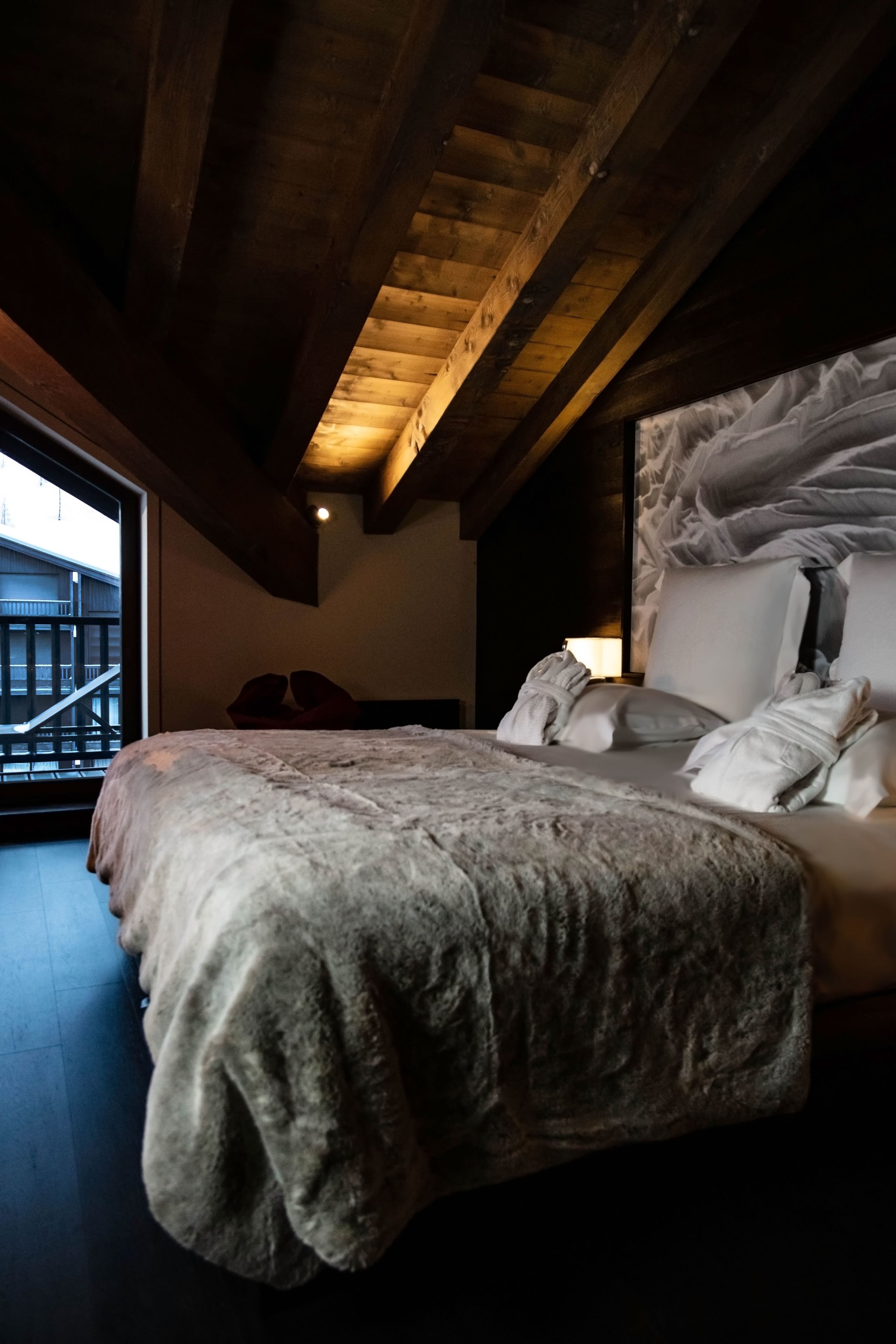 A bedroom with a large bed, wooden beams on the ceiling, and a view of a balcony.
