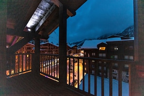 Un balcón de madera con vistas a una montaña nevada y un edificio iluminado al fondo.