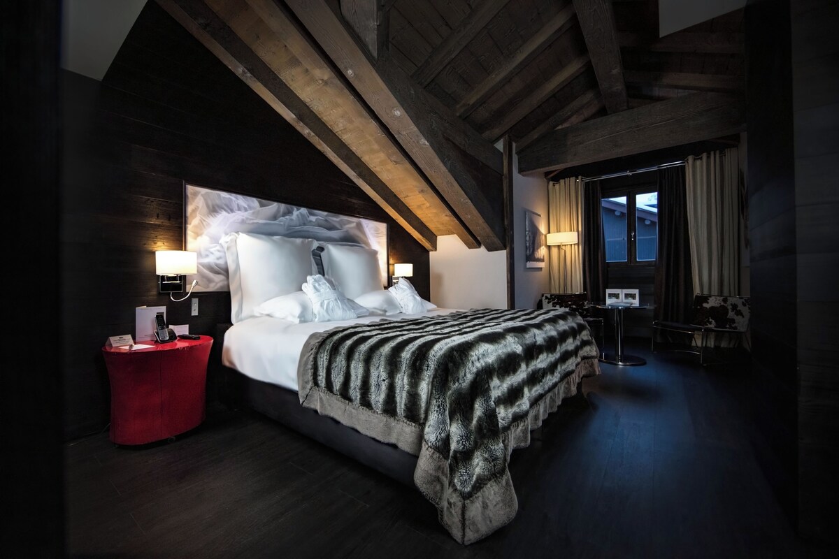 A modern bedroom with a large bed, a red side table, and a view of the outside.