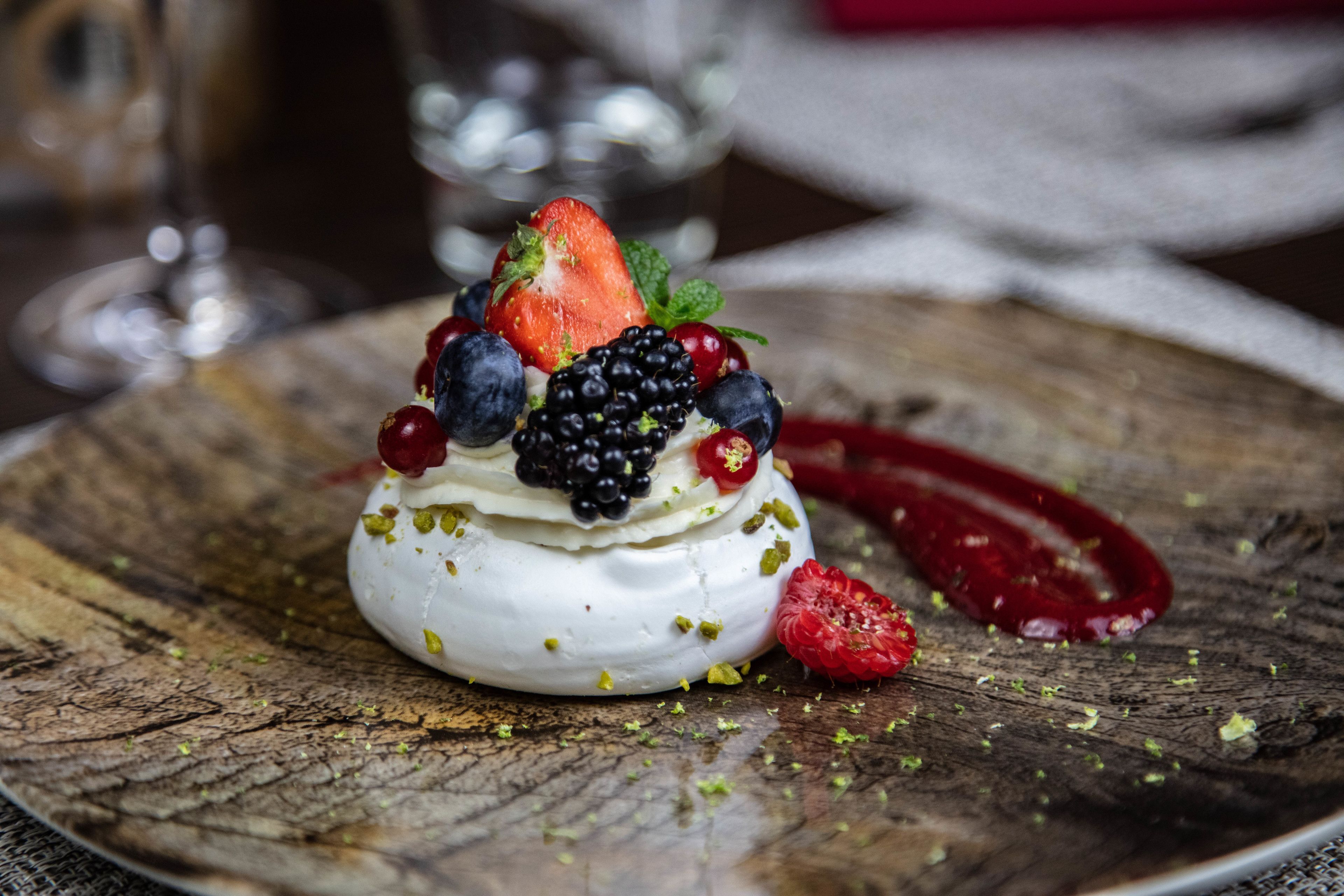 A dessert on a rustic wooden plate with a variety of berries and pistachios.