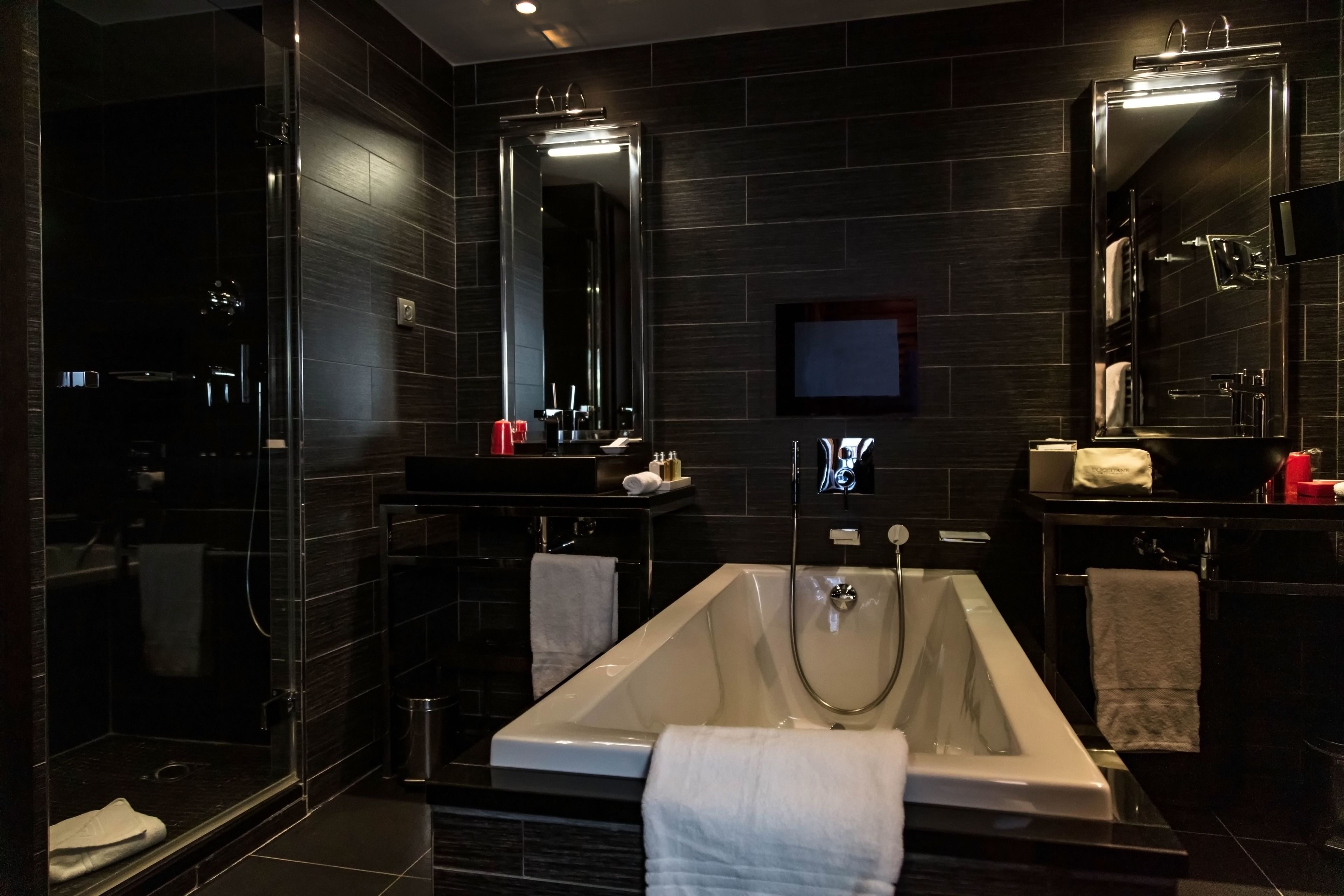 A modern bathroom with a large bathtub, a glass shower enclosure, and dark tiled walls.