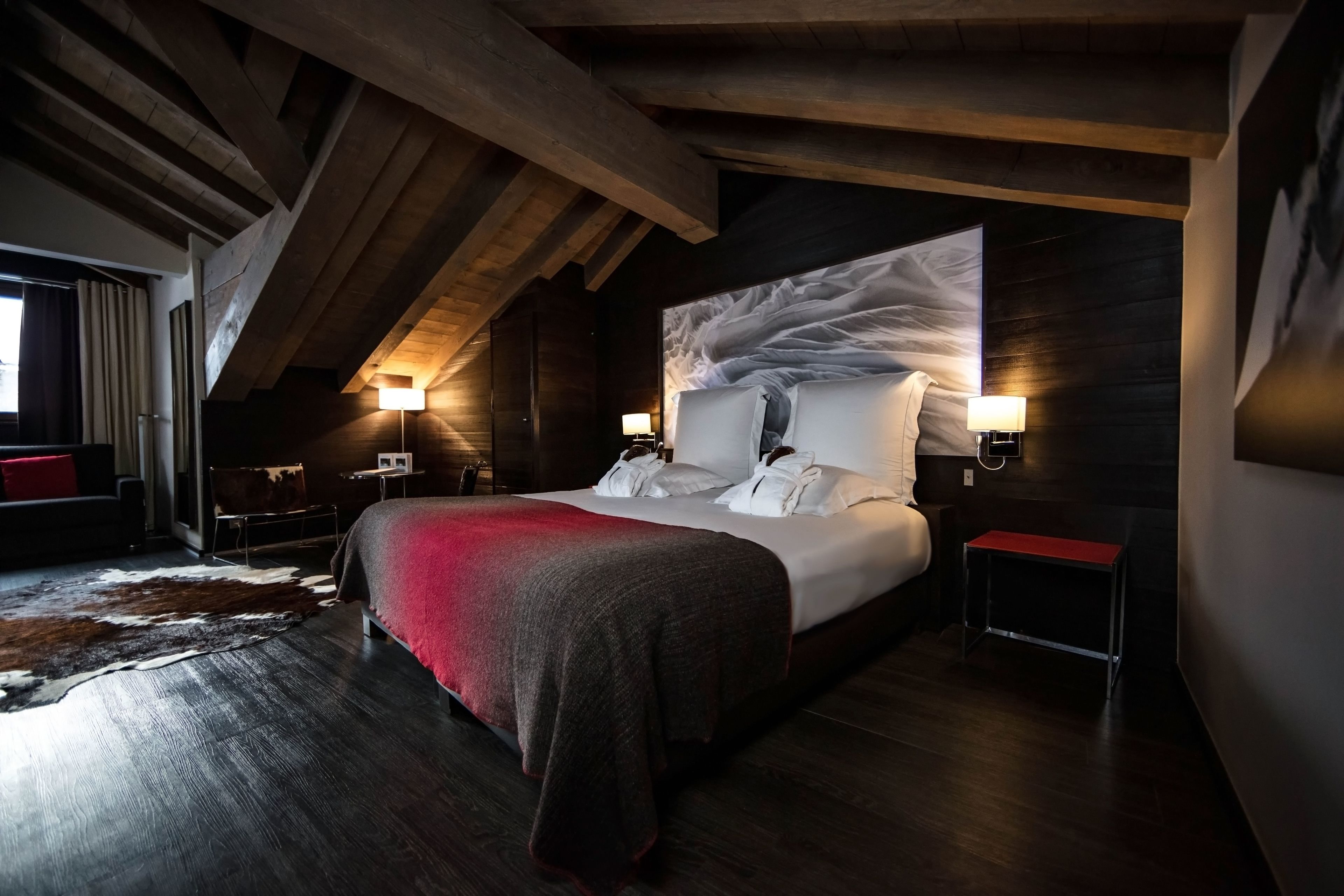 Un dormitorio moderno con una cama grande, vigas de madera, un tapiz de cuero de vaca y dos lámparas de noche.