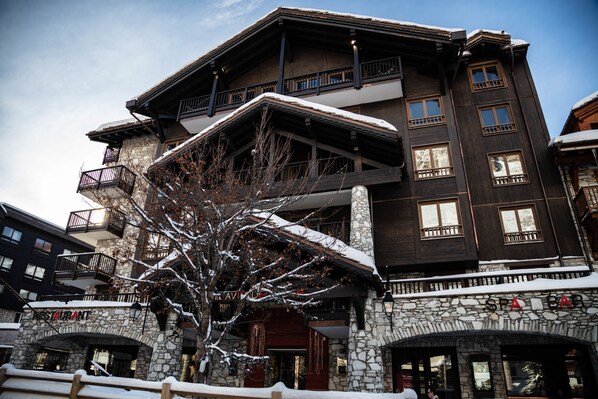 A multi-story building with stone and wooden architecture, featuring balconies and large windows. - Hôtel Avenue Lodge (Val-d'Isere)