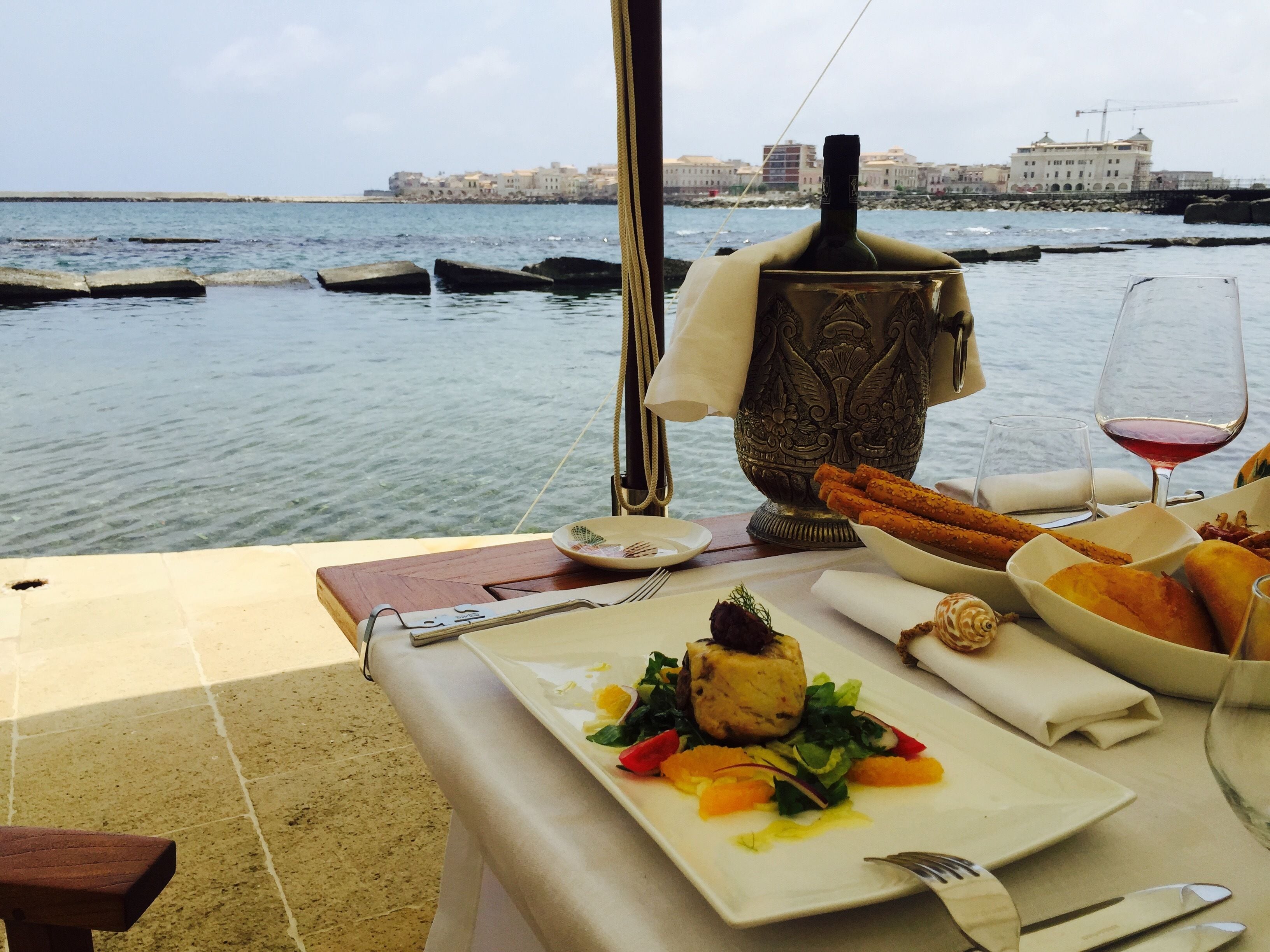 A table set for dining with a view of the sea and buildings in the background.