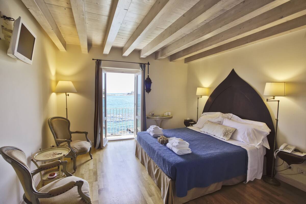 A bedroom with a bed, bedside lamps, a small table, and a chair.