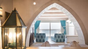 Acogedora habitación con vista al mar, que incluye un amplio arco, un farolillo y sofás azules con diseños.