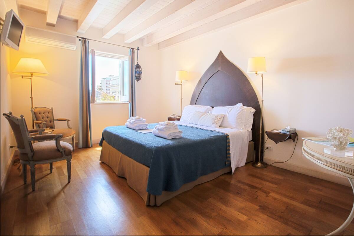 A hotel room with a bed, a chair, a desk, and a lamp.