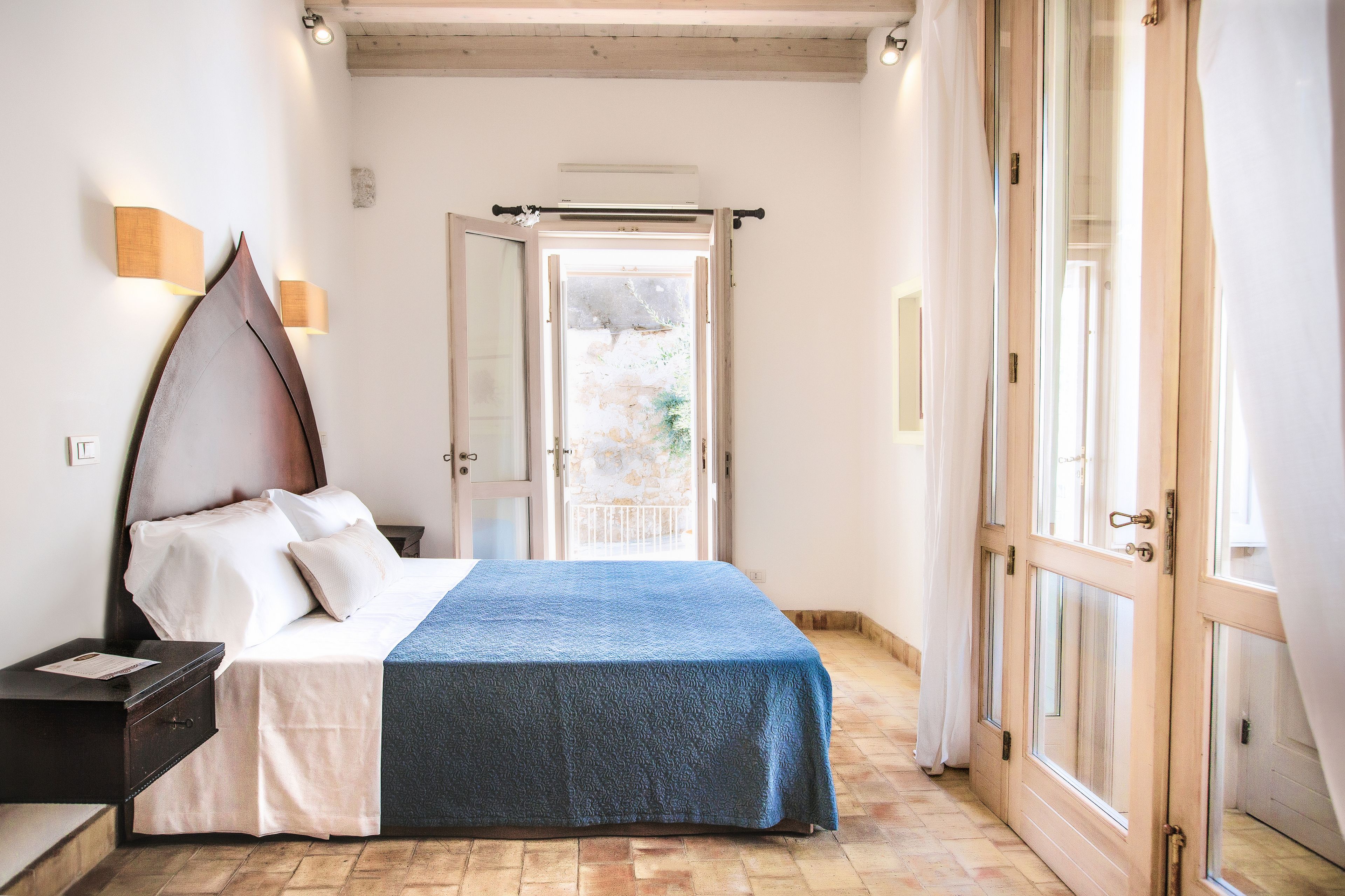 A bedroom with a bed, bedside table, and a view of the outside through a glass door.