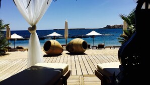 Una terraza de madera con sillones reclinables y sombrillas con vista a una playa.